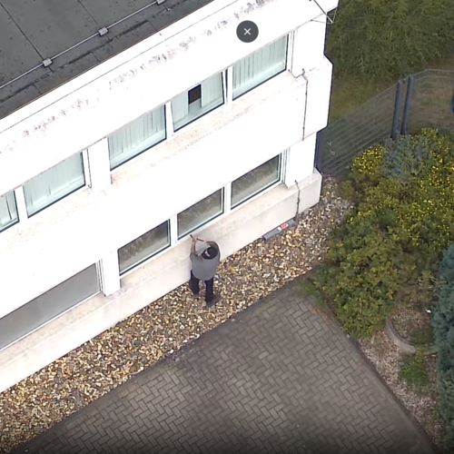 Eine maskierte Person schaut nach oben in die Kamera einer Flugdrohne.