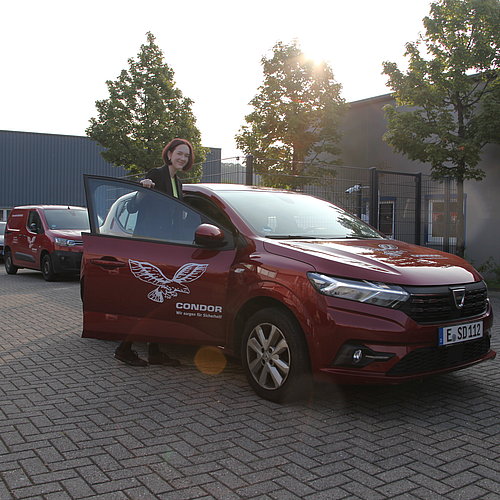 Eine Frau ist im Begriff in ein rotes Auto zu steigen. Auf der Autotür vor ihr ist das Logo des CONDOR Schutz- und Sicherheitsdiensts.