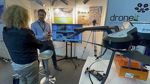Intergeo_2023_Joachim_Schlechtriem Ein Mann erklärt einer Frau eine Drohne.